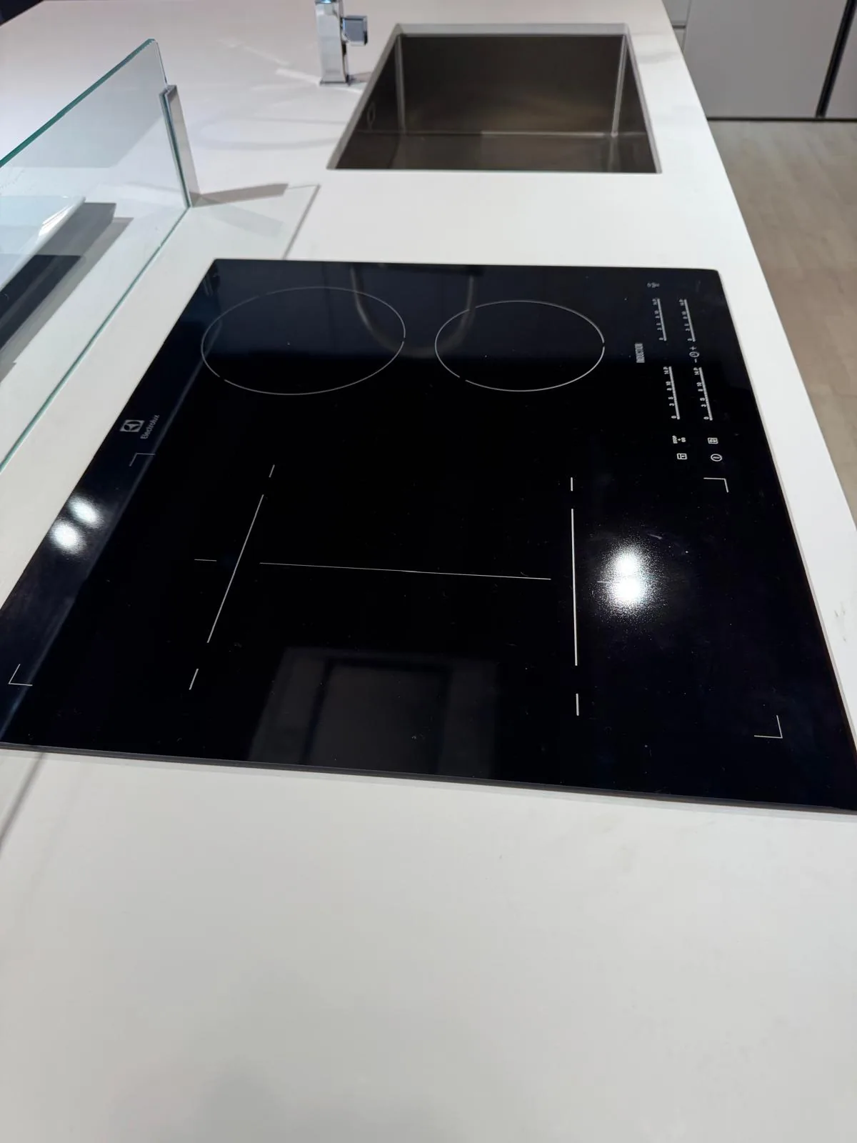 Piano cottura a induzione Electrolux incassato nel quarzo bianco, con alzatina in vetro e lavello sullo sfondo